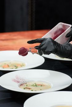 Chief serving fish cream soup with salmon, cheese and herbs in white soup bowls.