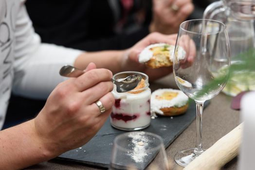 Woman eats dessert in a glass cup, with Jello, yogurt and topping served in a restaurant. Mini desserts.