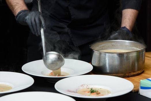 Chief serving fish cream soup with salmon, cheese and herbs in white soup bowls.