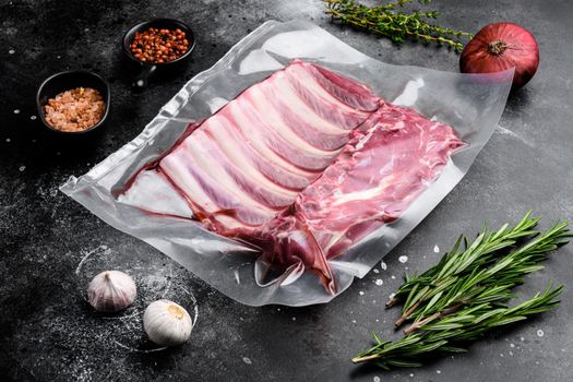 Supermarket packaged raw lamb rib rack set, on black dark stone table background