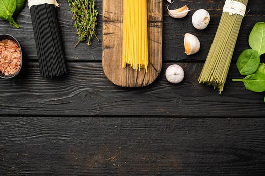 Dry colorful Italian pasta spaghetti with ingredients set, on black wooden table background, top view flat lay, with copy space for text