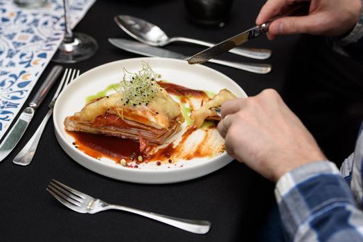 Man eating Francesinha, traditional Portuguese sandwich in a restaurant. National cuisine concept.