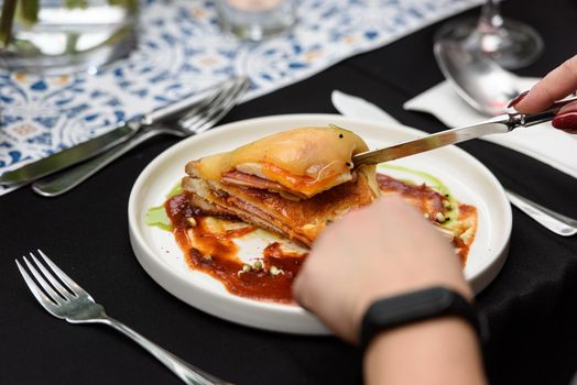 Man eating Francesinha, traditional Portuguese sandwich in a restaurant. National cuisine concept.