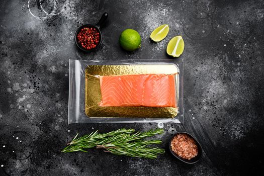 Vacuum packed salmon portion fillet set, with herbs, on black dark stone table background, top view flat lay, with copy space for text