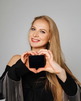 Beautiful middle-aged woman makeup artist holds shadows in her hands and looks at the camera smiling. Blond hair and a black jacket on a light background