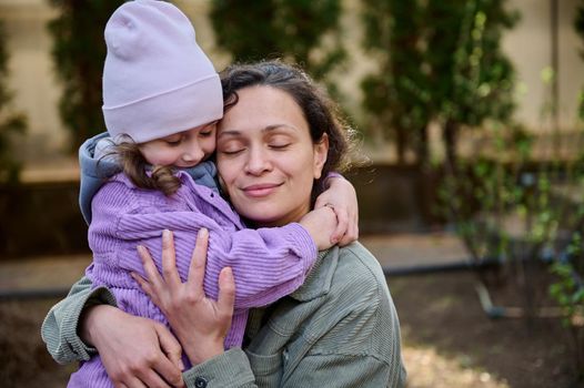 Beautiful woman mother hugging her lovely daughter while standing together in the backyard of her country house on an early spring day. Family relationships, Mother and Children protection Day