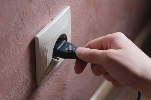 A female hand inserts an electric plug into a euro-format socket close-up.