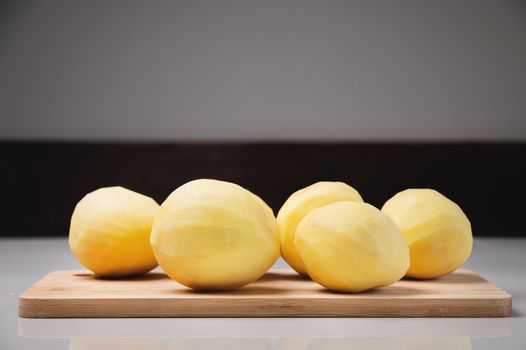 Close-up Several peeled potatoes on a wooden cutting board on a white table