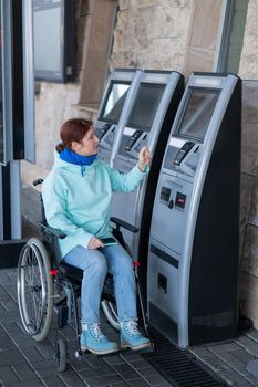 Caucasian woman in a wheelchair buys a train ticket at a self-service checkout