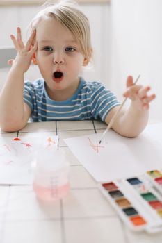 Child painting and drawing with watercolor paint at white table. Development of creative potential in children