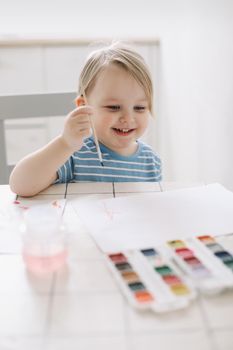 Child painting and drawing with watercolor paint at white table. Development of creative potential in children