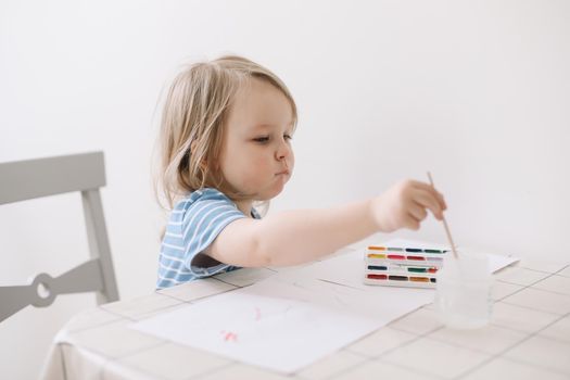 Child painting and drawing with watercolor paint at white table. Development of creative potential in children