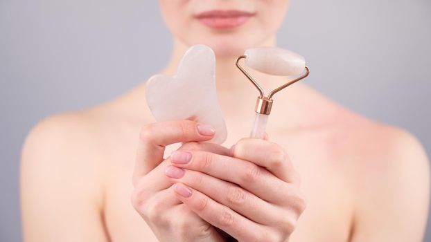 Caucasian woman holding pink roller massager and gouache scraper on white background