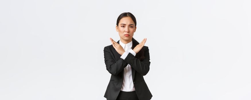 Serious-looking confident businesswoman in black suit showing cross gesture to forbid action, restrict, forbid or prohibit making any deals, stop working with client, white background. Time out.