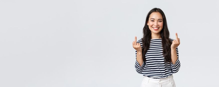 Lifestyle, beauty and fashion, people emotions concept. Unbothered and careless young happy smiling woman dont give a damn, showing middle fingers and feeling good, white background.