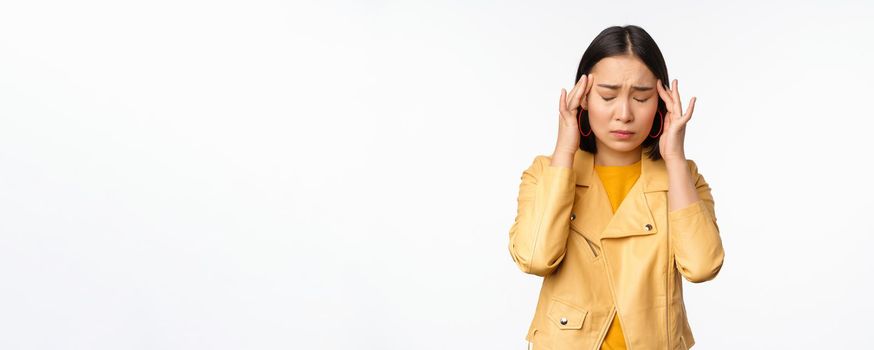 Image of asian woman massaging head temples with concerned face, suffering headache, migraine, standing over white background.