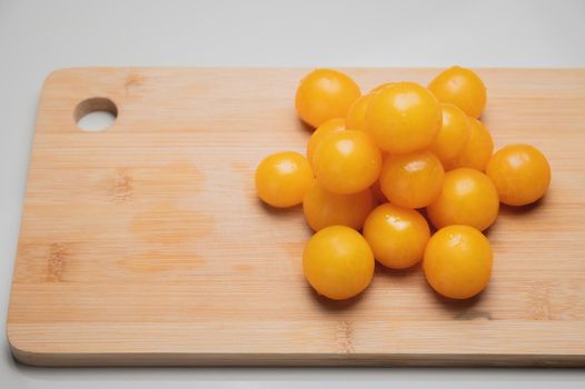 A heap of yellow cherry tomatoes on a wooden cutting board in the kitchen on a white table.