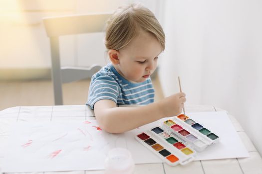 Child painting and drawing with watercolor paint at white table. Development of creative potential in children