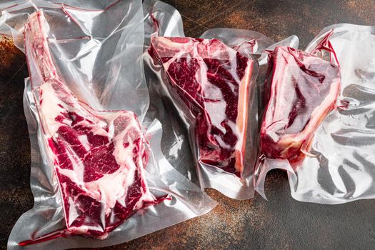 Raw beef dry aged steak vacuum sealed bag for sell set, tomahawk, t bone and club steak cuts, on old dark rustic background