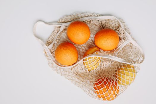 Lemons in reusable bag. Zero waste concept with string bag, mesh bag, grosery bag with fruits on white background, flat lay, top view, copy space.