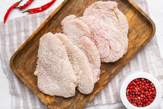 Raw chicken schnitzel in breadcrumbs, on white stone table background, top view flat lay