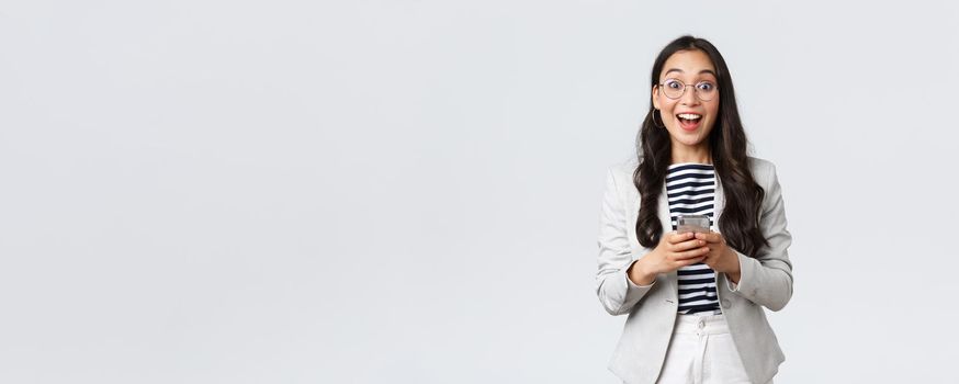 Business, finance and employment, female successful entrepreneurs concept. Cheerful happy asian businesswoman, office manager looking upbeat camera with smile, using smartphone.