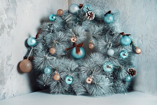 Round fir garland with snow, blue glitter balls and pine cones. Traditional Christmas decorative wreath over grey antique marble wall. Holiday interior details. New Year mood.