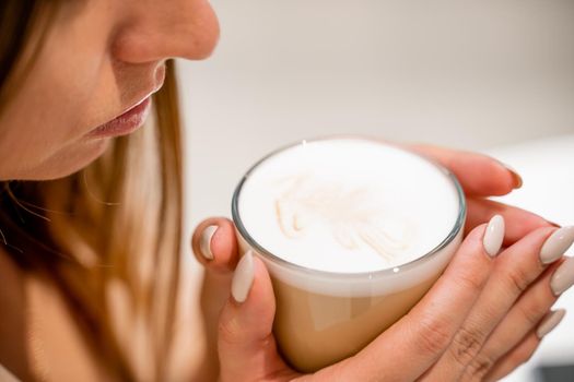 Close-up of beautiful female hands holding a large white cup of cappuccino. A woman is sitting in a cafe