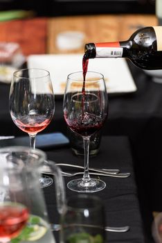 Pouring red wine into the glass against served table background