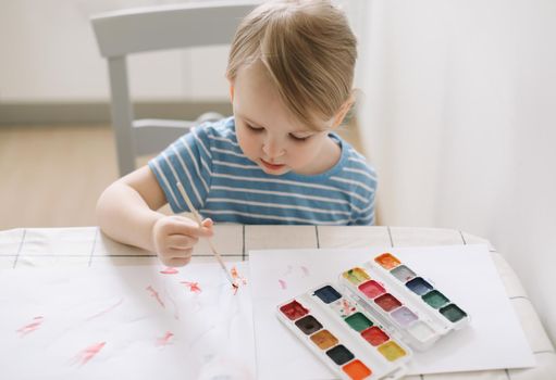 Child painting and drawing with watercolor paint at white table. Development of creative potential in children