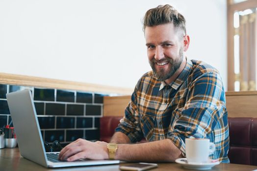 Portrait of a young man using his laptop while sitting in a cafe.