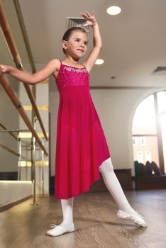 the charming little girl dreams of becoming a ballerina. The girl in the pink dress is dancing, holding on to the bar.Baby girl is studying ballet.