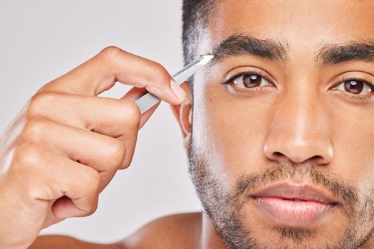 Shot of a young man plucking his eyebrows against a grey background.