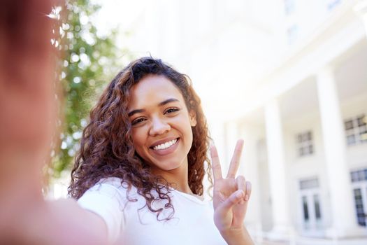 Shot of a female showing a peace gesture while taking a selfie outside.