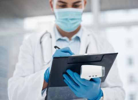 Shot of a young doctor writing down information while holding a thermometer in an office.