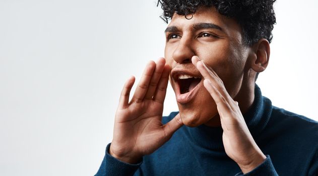 Studio shot of a young man yelling against a grey background.