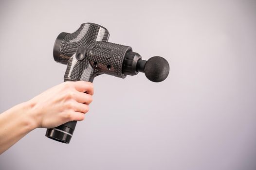 Close-up of a female hand with a portable massager gun on a white background