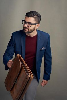 Studio shot of a handsome young man carrying a bag against a grey background.