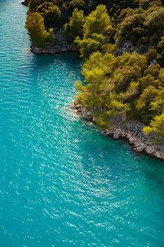 azure water of the lake and slopes of mountains on a background, coast line, green trees, sun light. High quality photo