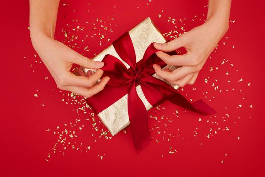 Female hands tying a bow on gift box with wine ribbon on red background. Concept of a gift for the holidays, birthday, christmas Flat lay, top view