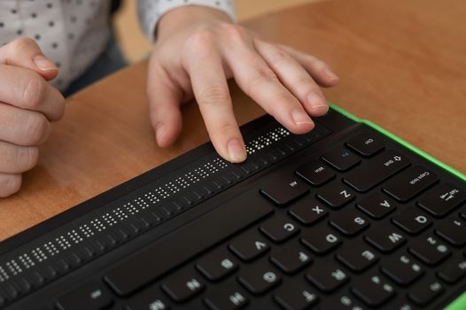 A blind woman uses a computer with a Braille display and a computer keyboard. Inclusive device