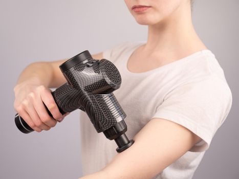 Caucasian woman uses a massager gun for pain in the muscles of the arm