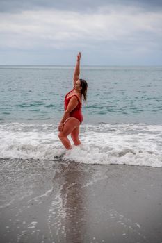 Woman in a bathing suit at the sea. A fat young woman in a red swimsuit enters the water during the surf.