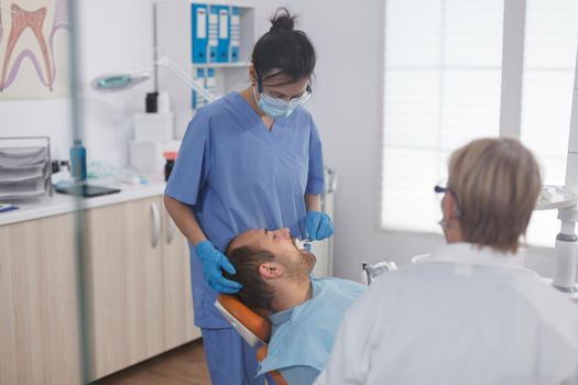 Dental woman nurse applying anesthesia with cotton swab before stomatological procedure in orthodontic office. Medical team discussing treatment against caries infection during dentistry examination