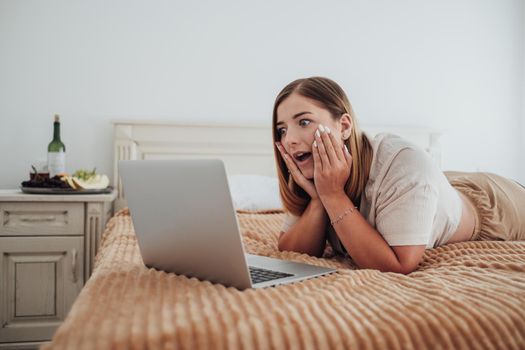 Young Caucasian Woman Showing Surprise Emotion While Watching Laptop on Bed of Hotel Room