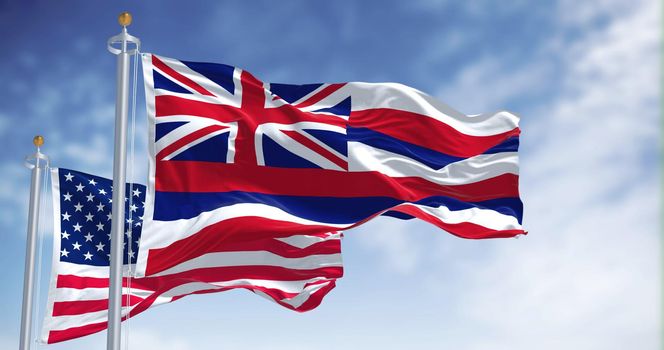 The Hawaii state flag waving along with the national flag of the United States of America. In the background there is a clear sky. Hawaii is a western state of the United States