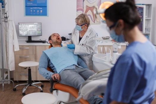 Dentist doctor woman with face mask using dental tools while checking patient mouth analyzing oral infection during stomatological consultation in dentistry office room. Concept of orthodontist team