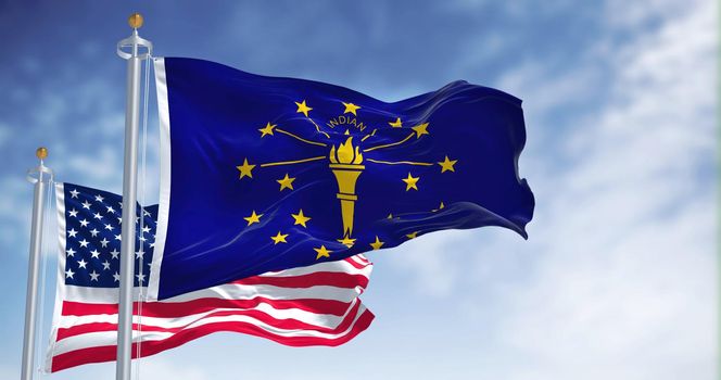 The Indiana state flag waving along with the national flag of the United States of America. In the background there is a clear sky. Indiana is a U.S. state in the Midwestern United States