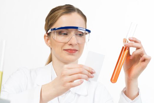 Beautiful young woman scientist in protective goggles looking at test tube with liquid in hand. Laboratory assistant conducts chemical experiment. Pharmaceutical research and medicaments testing.