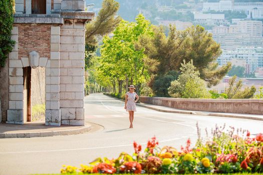 a bright beautiful girl in a light dress and hat walks along the streets of Monaco in sunny weather in the summer, luxury apartments of Monte Carlo on background. High quality photo
